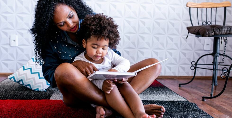 mãe e filho sentandos no chão lendo livro juntos representando o desenvolvimento da inteligência emocional infantil