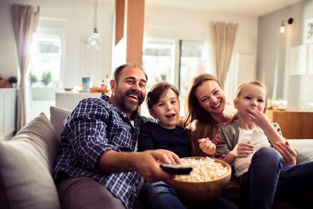 Imagem de uma família sentada no sofá e assistindo TV