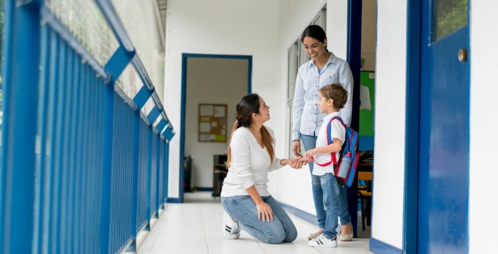 Imagem de uma criança na porta de uma sala de aula com duas adultas