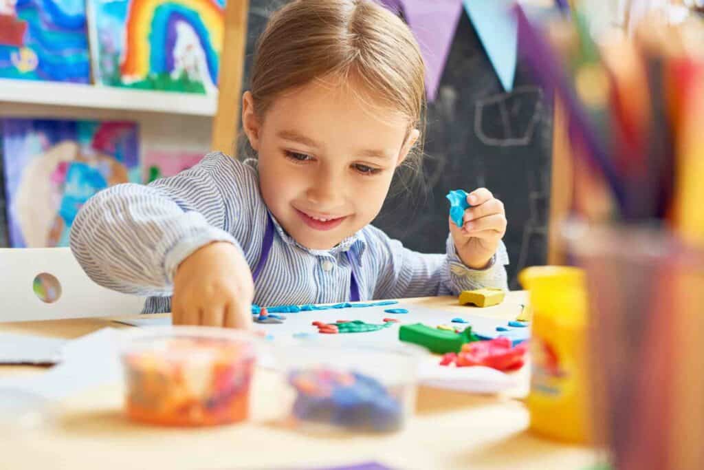 menina brincando com massinha em cima da mesa representando a importância da arte no desenvolvimento infantil