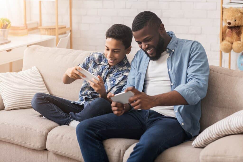 pai e filho sentados no sofá segundo celular aprendendo como jogar pókemon