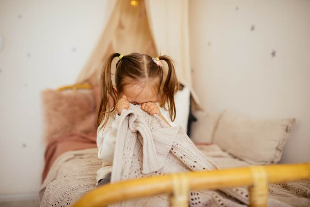 criança com medo em cima da cama tampando o rosto com um lenço