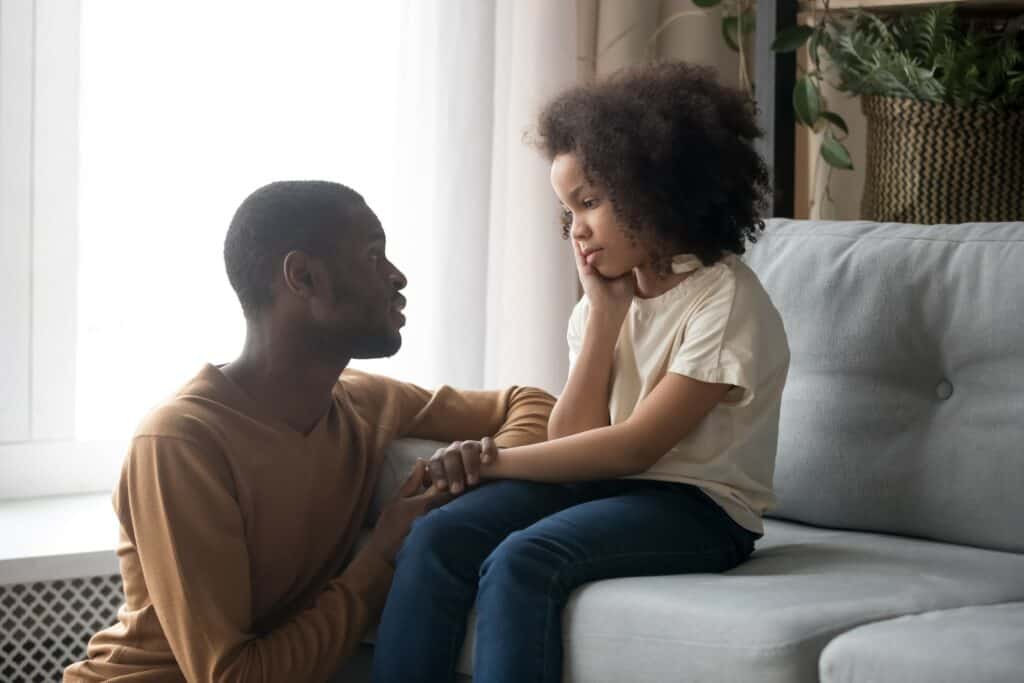 pai e filha sentada no sofá da sala conversando sobre como lidar com a frustração