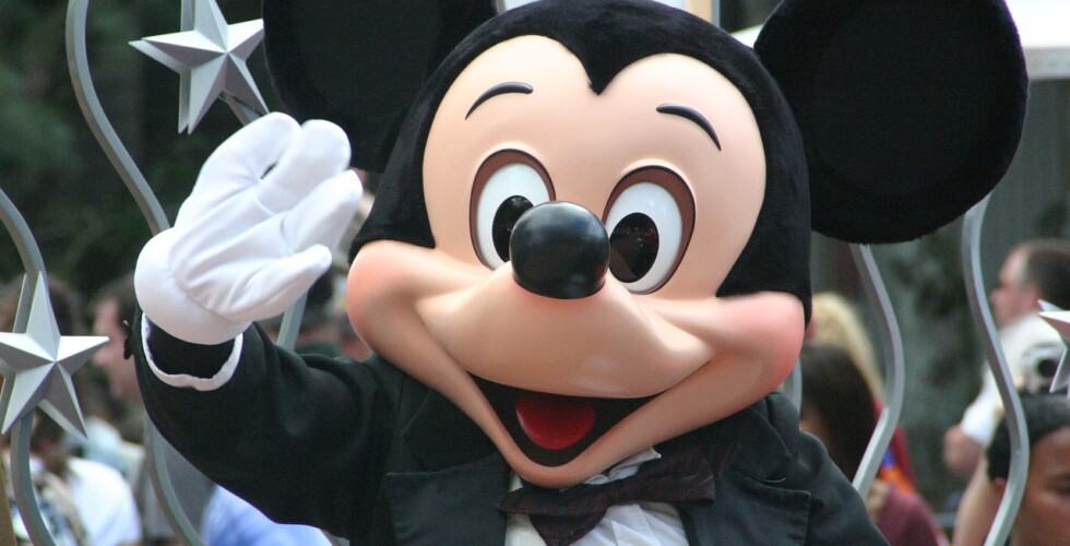 Imagem do personagem Mickey Mouse da Disney. Ele está acenando para quem tira a foto.