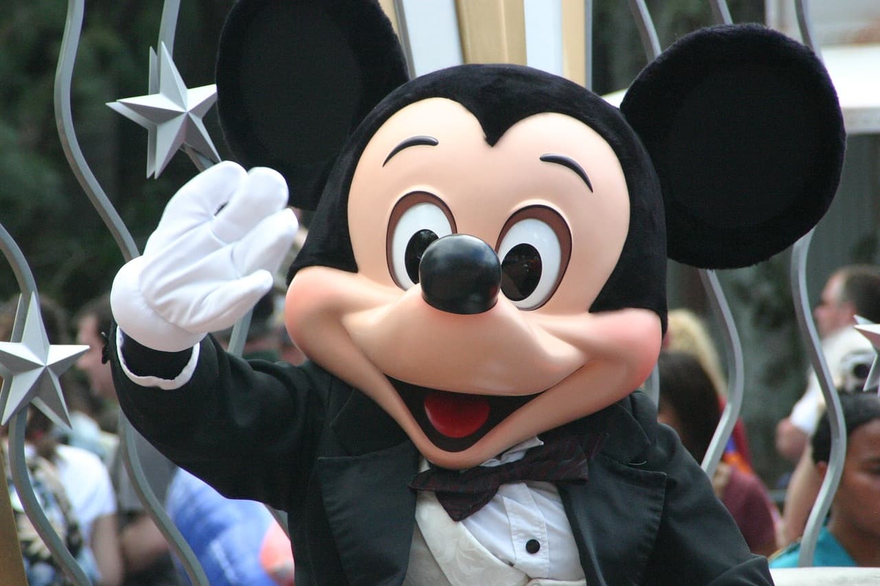 Imagem do personagem Mickey Mouse da Disney. Ele está acenando para quem tira a foto.