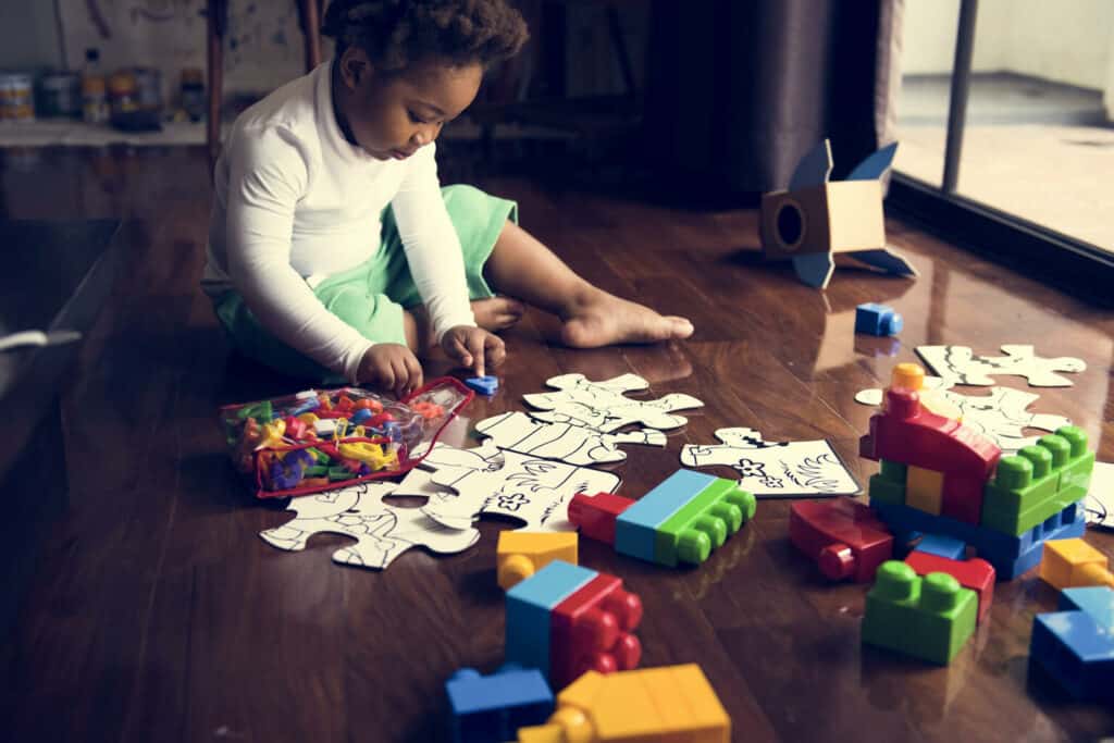 Imagem de uma criança montando um quebra-cabeça no chão.