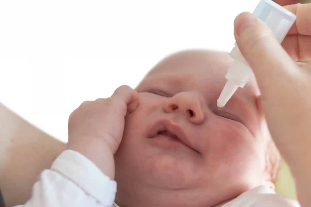 Imagem de uma mão pingando nitrato de prata no olho de uma criança recém-nascida.