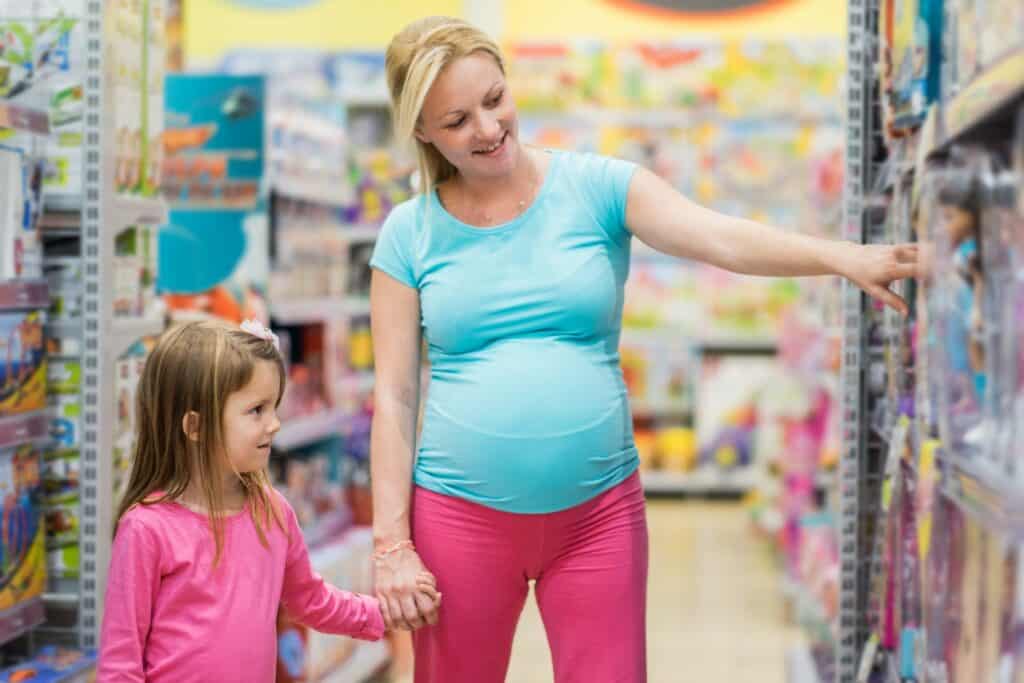 Imagem de uma criança com a sua mãe grávida escolhendo brinquedos numa loja.
