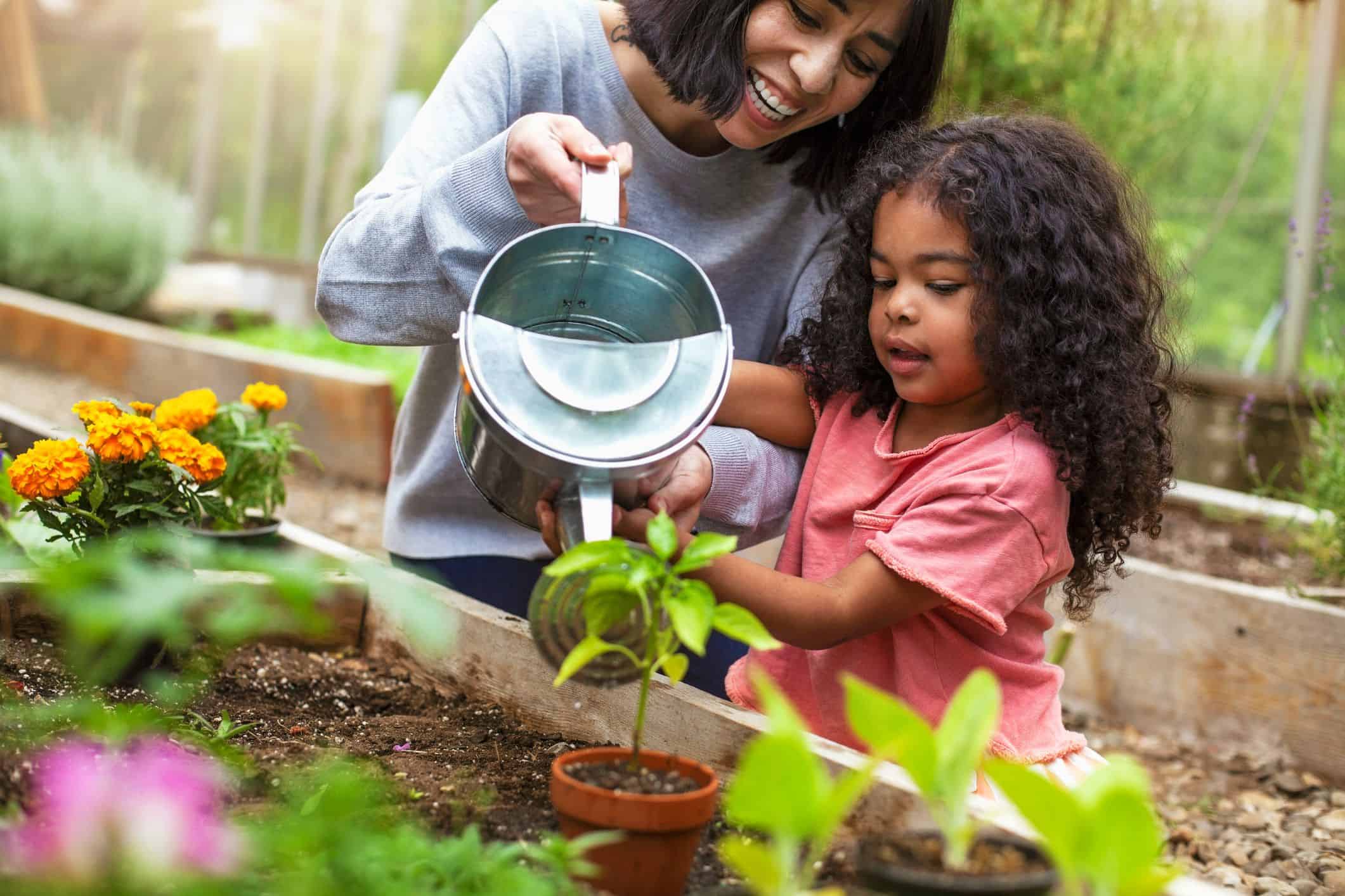 mãe e filha regando plantas em horta para crianças