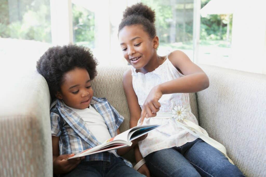 Imagem de duas crianças se divertindo enquanto leem um livro.