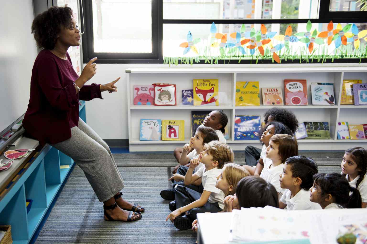 professora em sala de aula explicando em frente ao quadro com crianças sentadas a sua frente