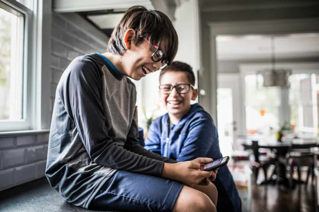 meninos sentados na sala de casa rindo enquanto olham o celular representando a amizade infantil