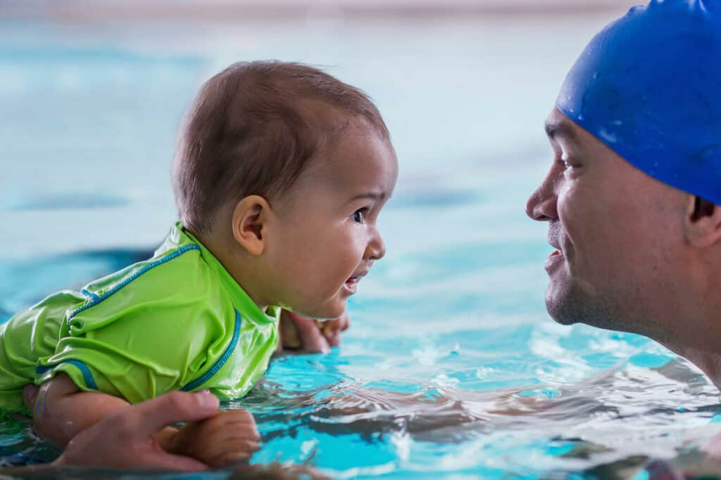 pai aprendendo como ensinar um bebê a nadar dentro da piscina