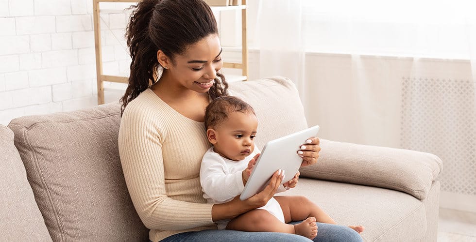Imagem de uma mulher com um bebê no colo assistindo desenho em tablet