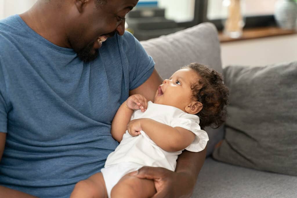 pai negro segurando seu bebê sentado ao sofá comemorando o primeiro dia dos pais