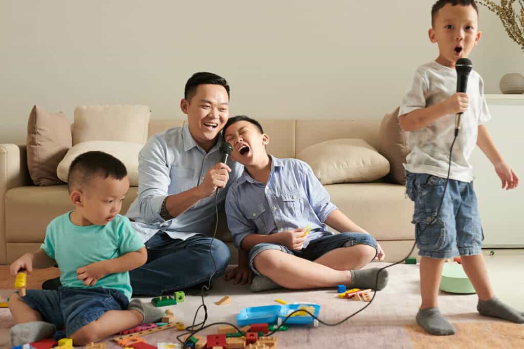 pai e filhos cantando karaoke na sala, uma das brincadeiras legais para fazer em casa