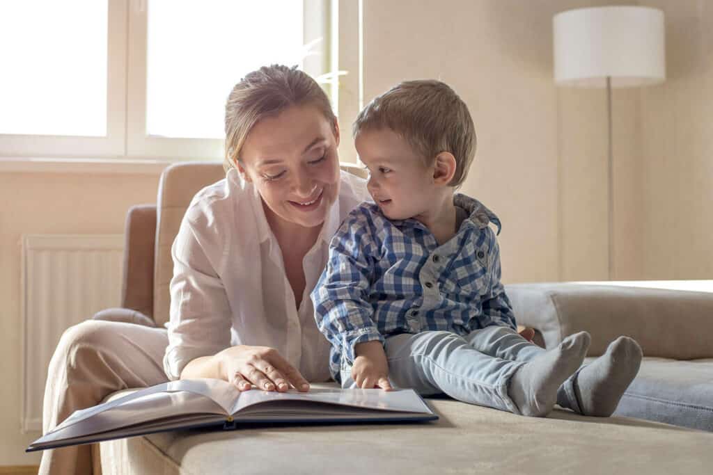 mãe estimulando a leitura para bebês lendo para seu filho em cima do sofá
