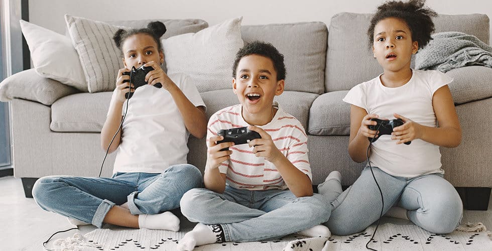 três crianças sentadas no chão da sala segurando controle jogando os melhor jogos do xbox one