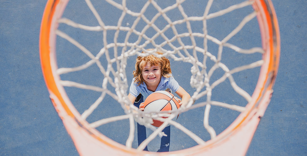criança descobrindo como jogar basquete enquanto arremesa bola na cesta