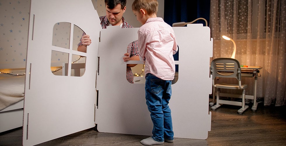 Imagem de um adulto e uma criança montando uma casinha de papelão
