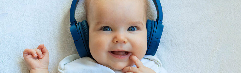 neném menino com fone de ouvindo sorrindo enquanto escuta música para bebês
