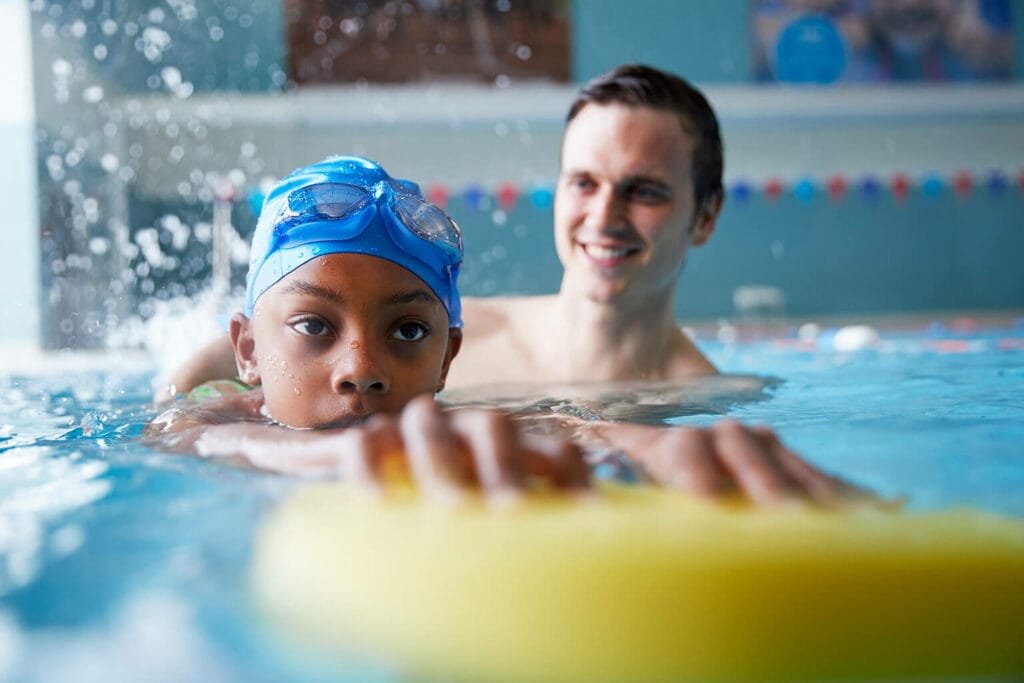 Imagem de um professor de natação infantil ajudando uma criança