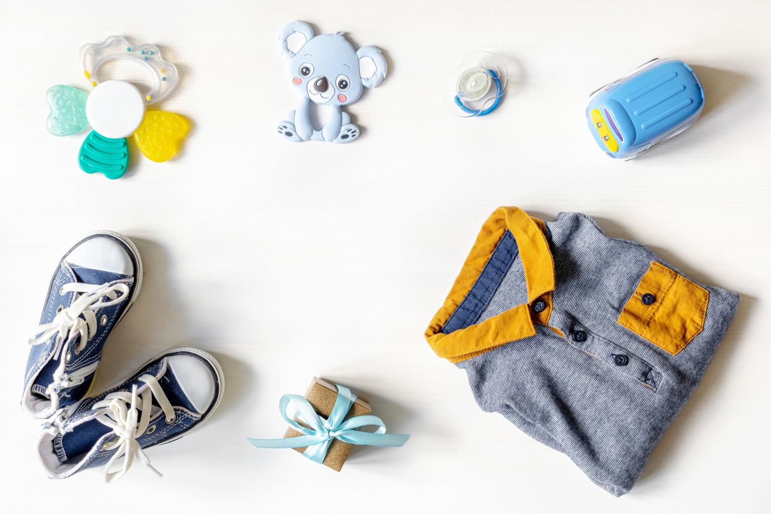 roupinha, tenis e brinquedos de bebê em cima de superfície branca representando presente para recém-nascido