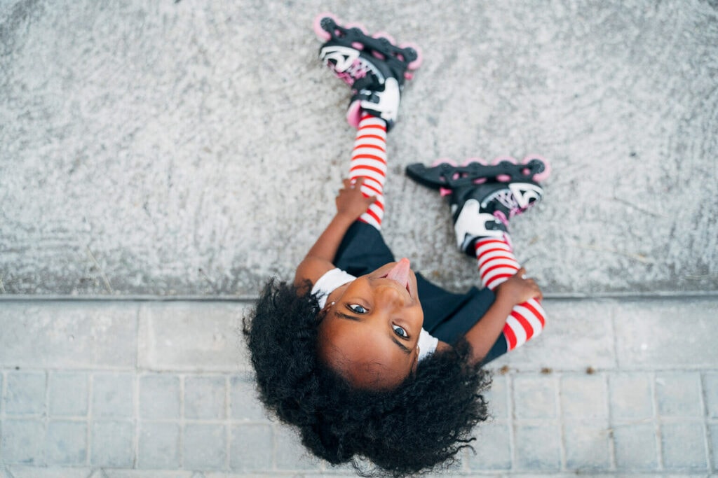 menina olhando pra cima com língua pra fora sentada com patins no pé