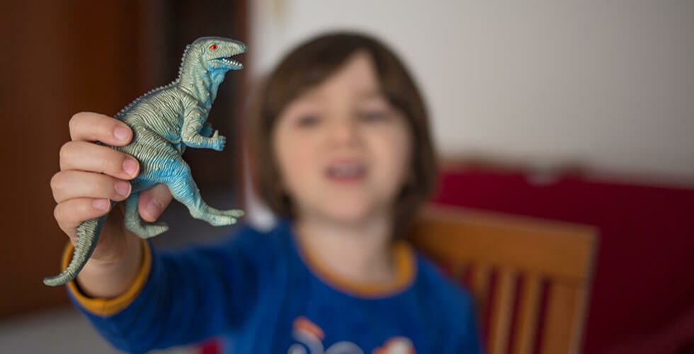criança segurando dinossauro de brinquedo representando filmes de dinossauros
