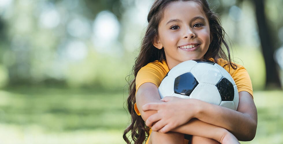 Imagem de uma menina segurando uma bola de futebol