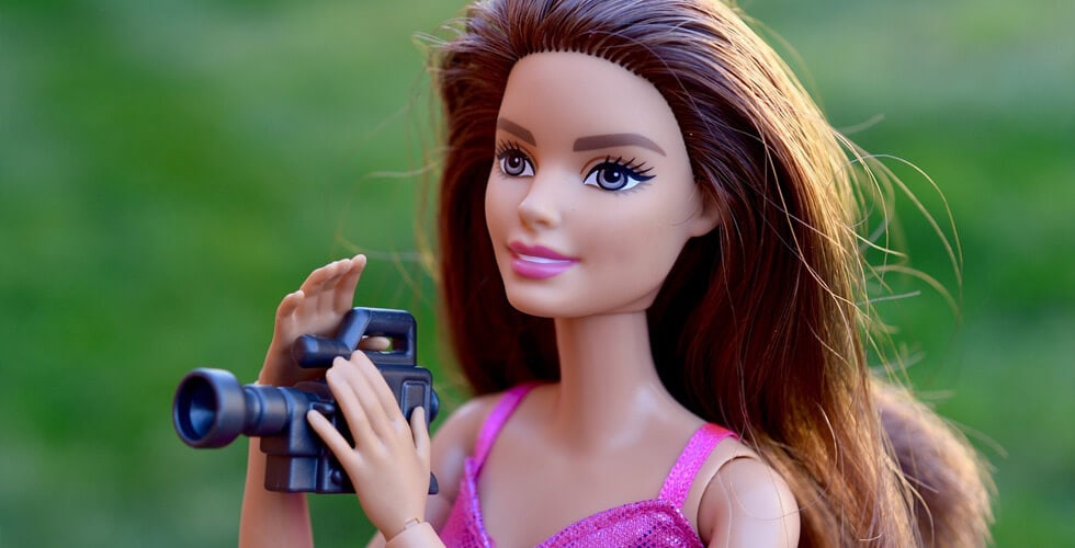 Imagem de uma boneca Barbie com uma câmera na mão