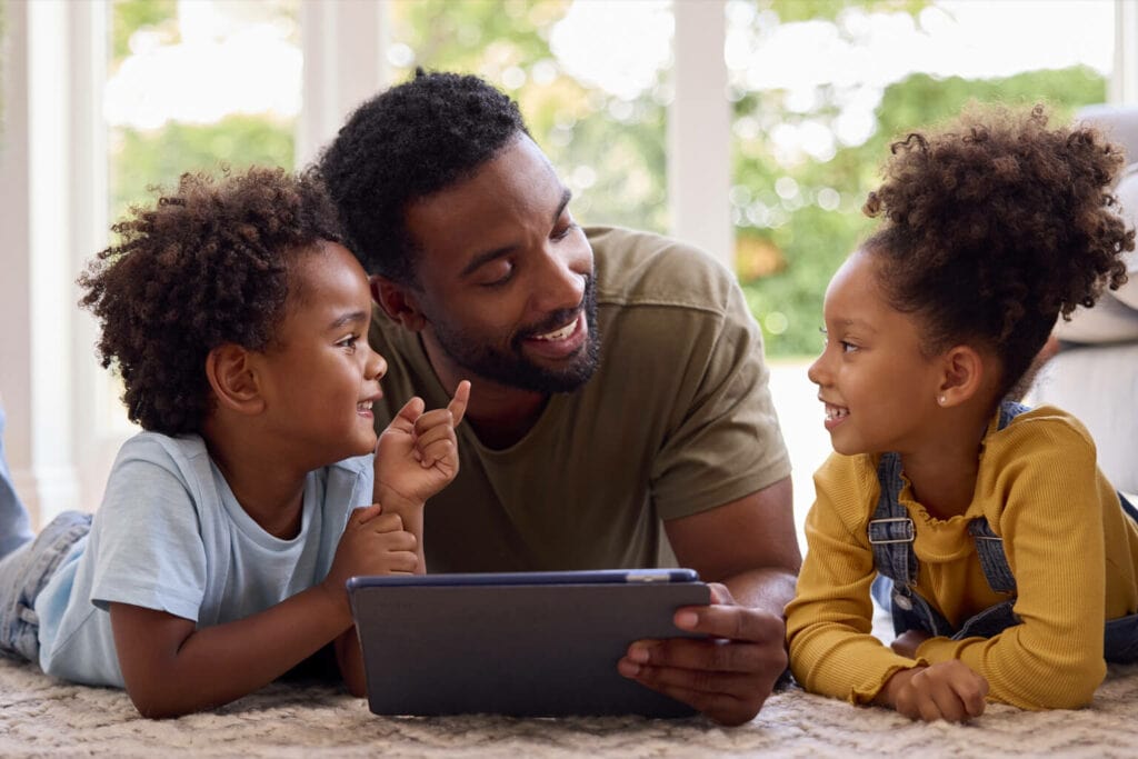 Imagem de um adulto vendo algo no tablet com duas crianças