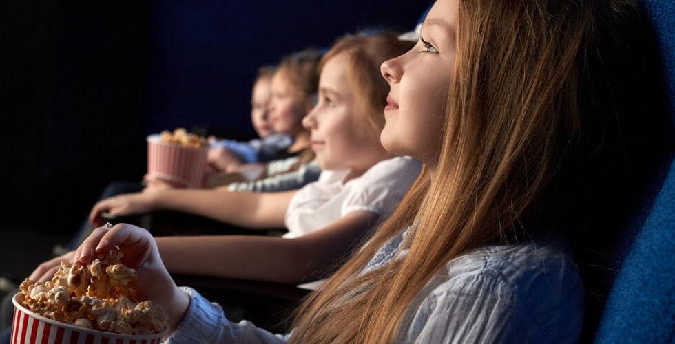 Imagem de crianças sentadas numa sala de cinema e segurando pipocas