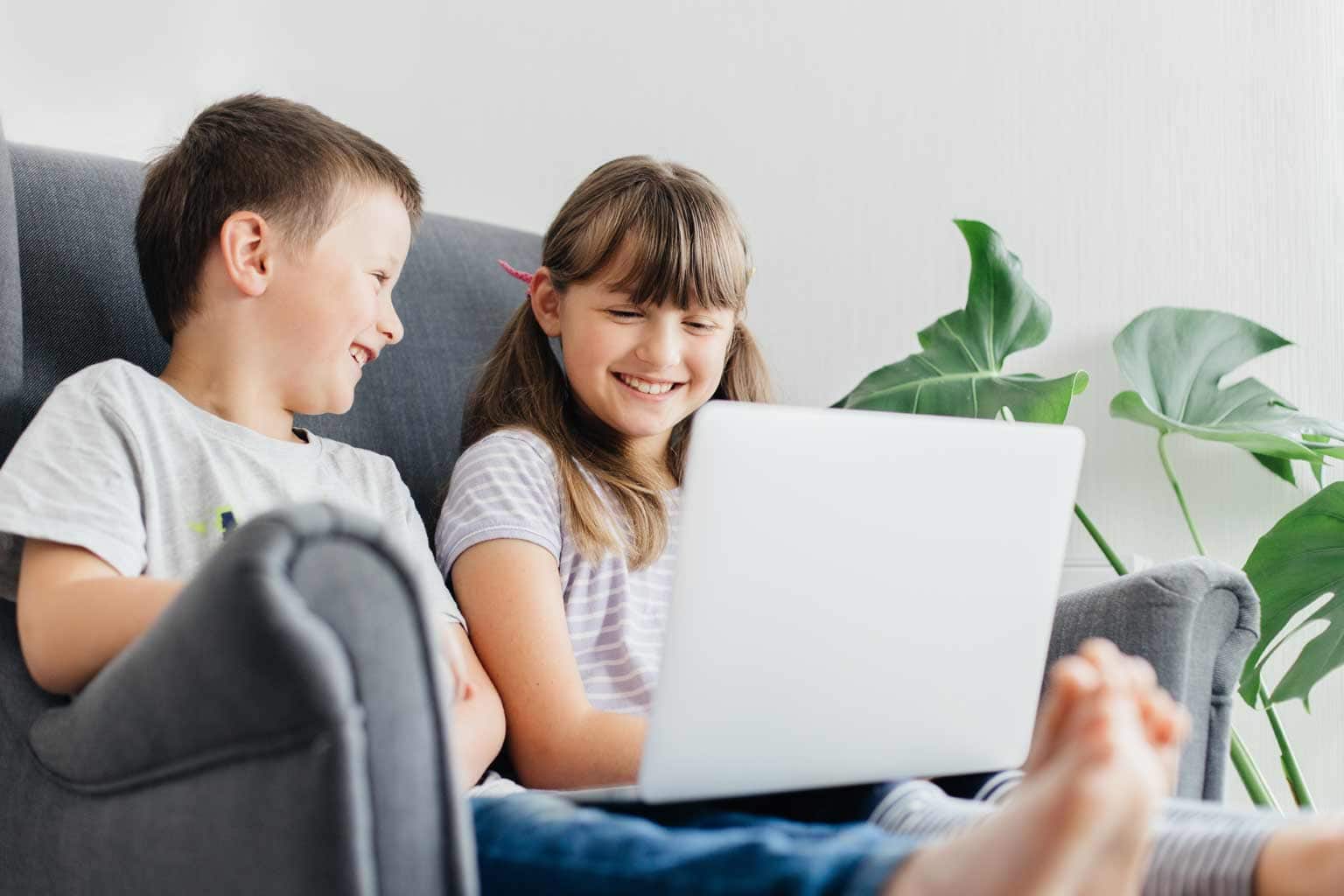 crianças sentadas no sofá sorrindo para notebook no colo representando o que é youtuber infantil