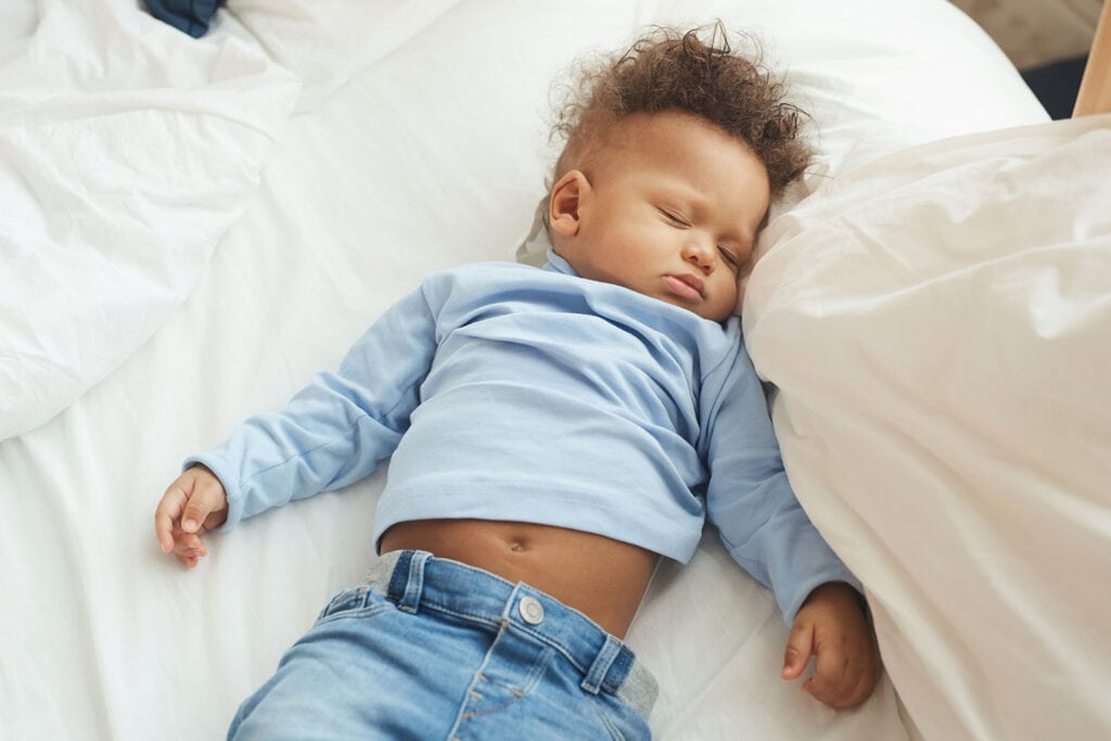 Imagem de um bebê dormindo em uma cama de lençóis brancos