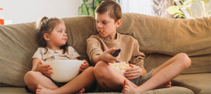 Imagem de duas crianças comendo pipoca em frente a TV