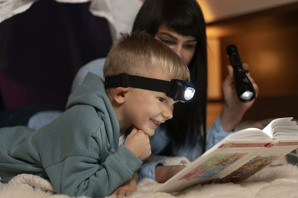 mãe e filho usando lanterna para ler história para criança dormir