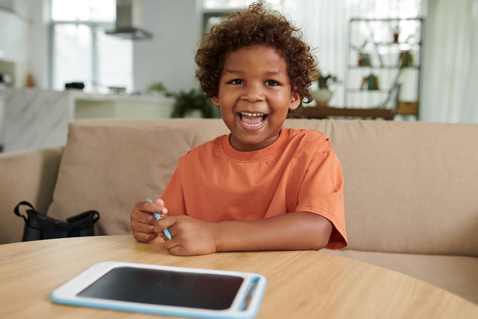 menino afrodescendente sorrindo para camera em frente a tablet na mesa representando crianças na internet