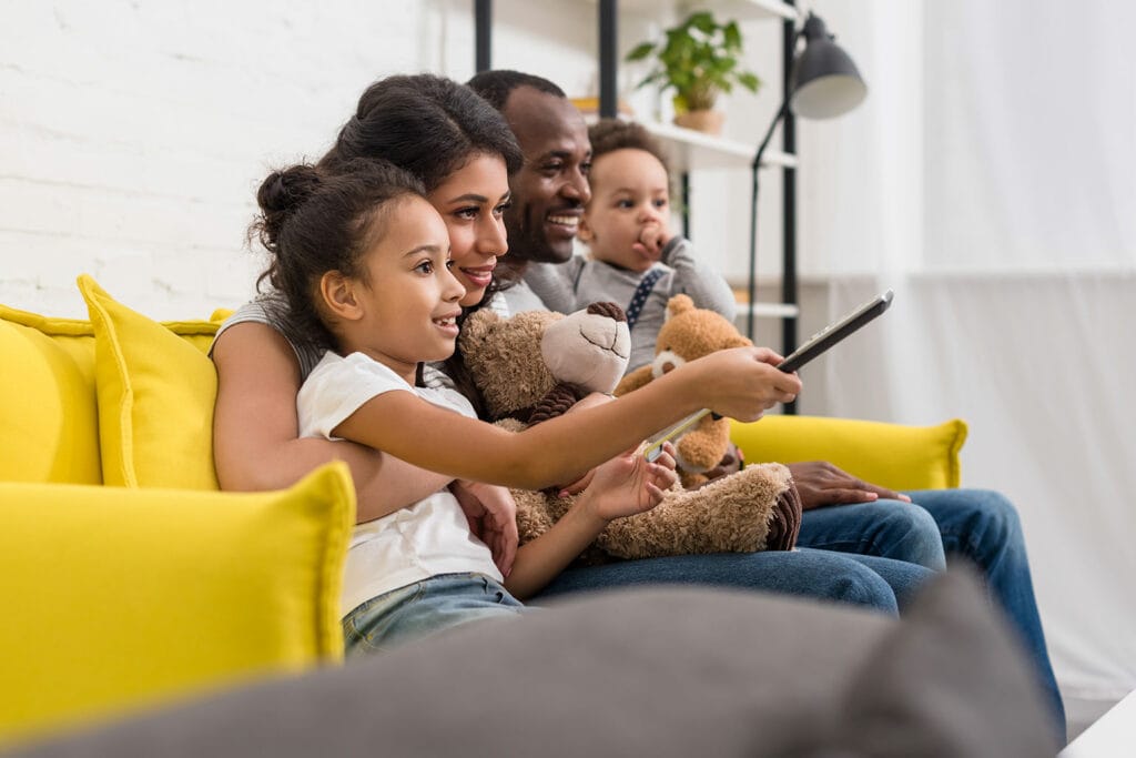 pessoas sentadas no sofá segurando controle remoto enquanto procuram filme para assistir em família