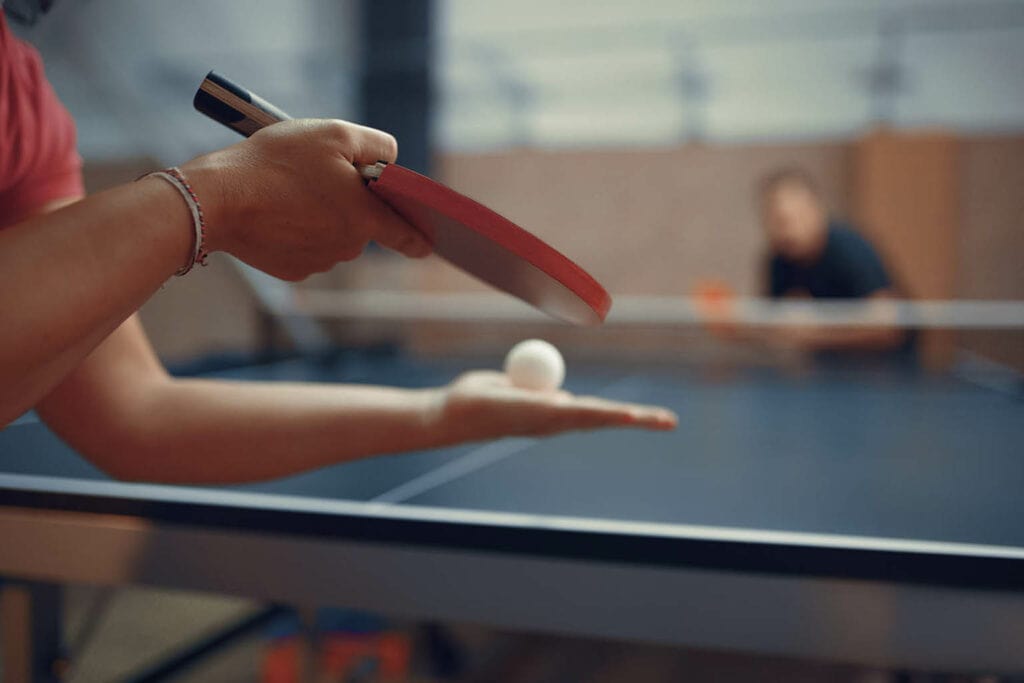 jogador se preparando para sacar com raquete e bolinha na mão representando as regras do tênis de mesa