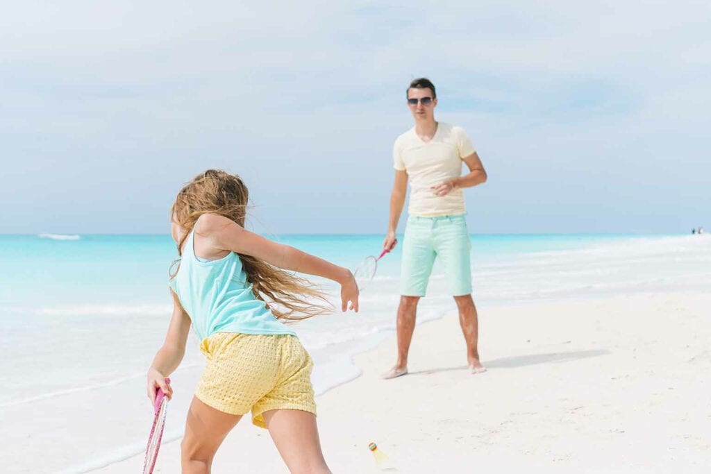Imagem de uma criança jogando beach tennis com um adulto