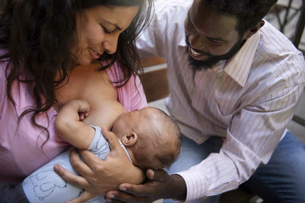 mãe dando de mamar ao bebê enquanto o pai incentiva representando a amamentação materno exclusiva
