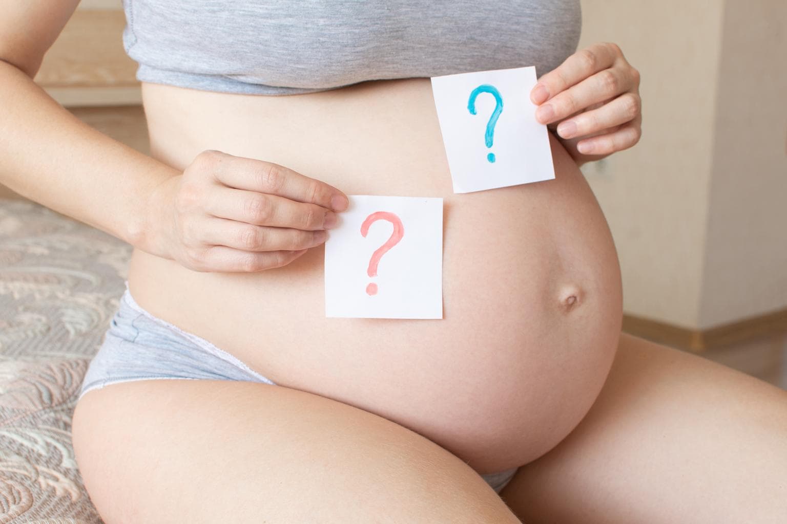 Mulher grávida segurando ponto de interrogação azul e rosa em papel 