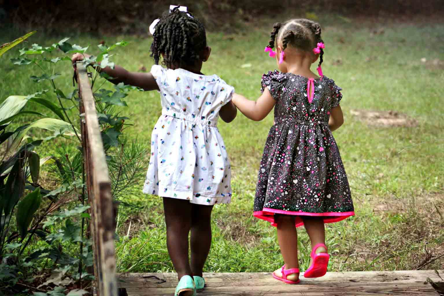 meninas de mão dada em frente a terreno com grama representando o dia da amizade