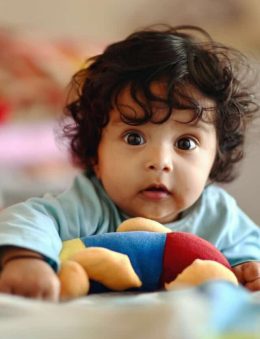 Imagem de um bebê de cabelos escuros segurando um brinquedo